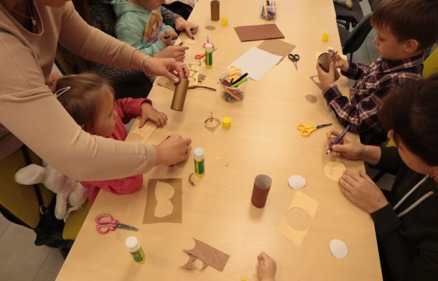 dzieci z rodzicami wycinają i kleją przy stołąch