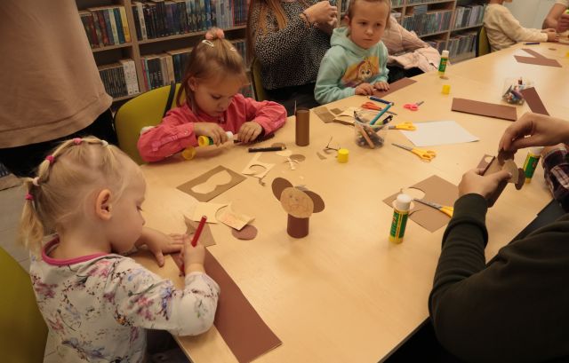 dzieci z rodzicami wycinają i kleją przy stołąch
