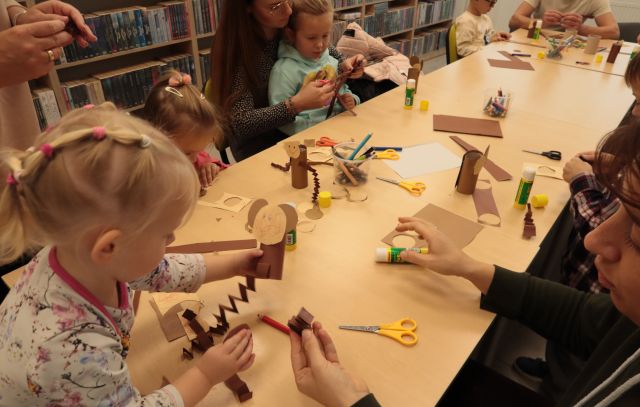 dzieci z rodzicami wycinają i kleją przy stołąch