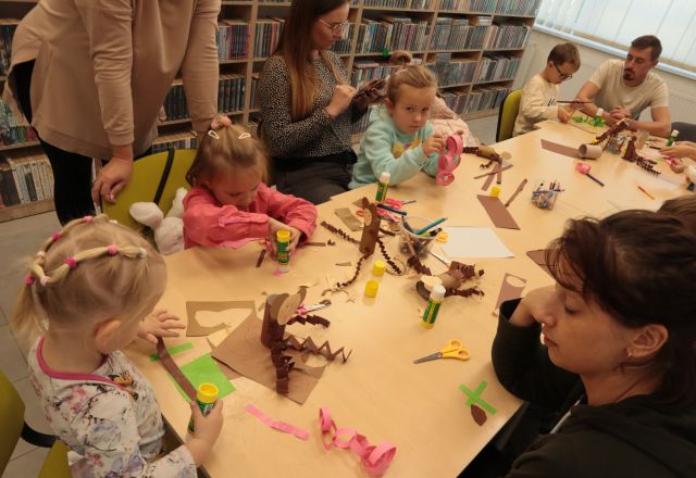 dzieci z rodzicami wycinają i kleją przy stołąch