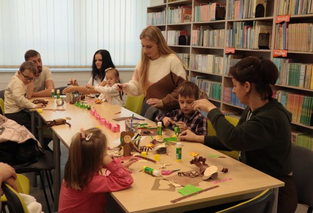 dzieci z rodzicami wycinają i kleją przy stołąch