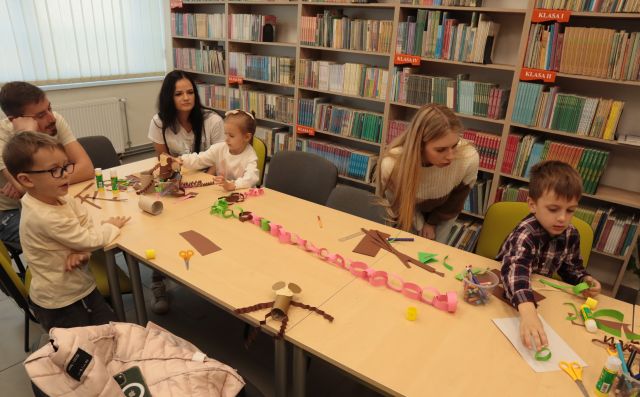 dzieci z rodzicami wycinają i kleją przy stołąch