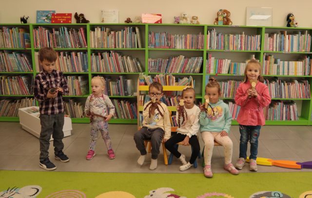 dzieci pozują do zdjęcia z wykonanymi przez siebie zwierzątkami z papieru, w tle regały z książkami