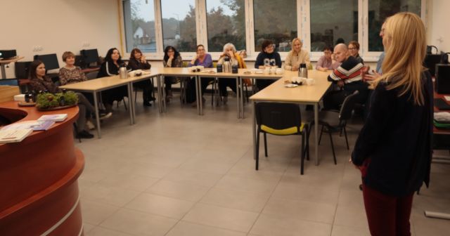 12 uczestników warsztatów siedzi przy stołach ustawionych w literę L