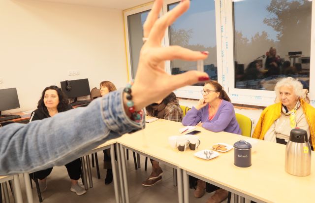 na zdjęciu dłonie trzymające malutką fiokkę, w tle uczestnicy spotkania siedzący przy stołach