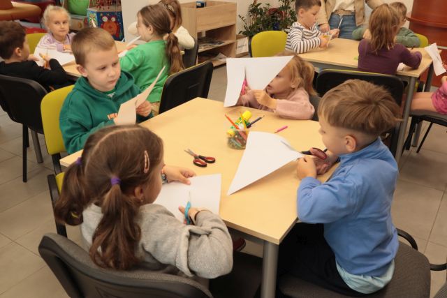 dzieci siedzą przy stoliku i wycinają z kartek