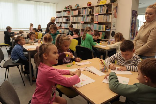 dzieci rysują przy stolikach, w tle regały z książkami