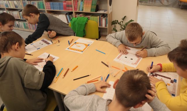 6 chłopców przy stołach koloruje ilustracje na kartkach