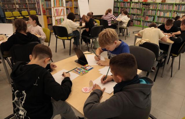 18 dzieci siedzących przy stolikach rysuje na krtkach