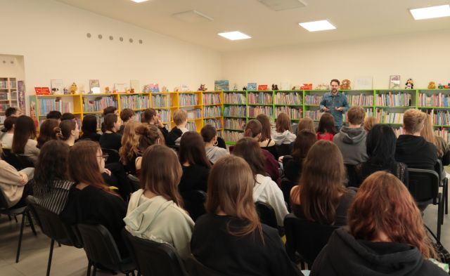 młodzież siedzi na krzesłach, w tle autor i regały z książkami