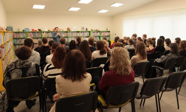 młodzież siedzi na krzesłach, w tle autor i regały z książkami