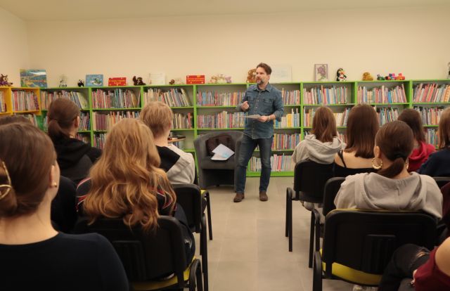 młodzież siedzi na krzesłach, w tle autor i regały z książkami