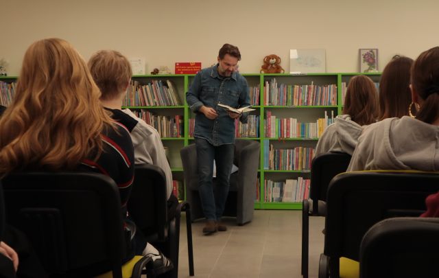 autor pochylony nad książką, w tle regały z książkami