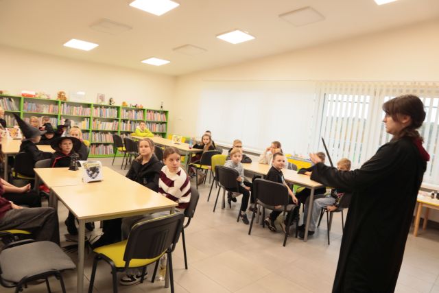 uczestnicy siedzą przy stołach w różnych strojach z Harry'ego Pottera, w tle regały z książkami