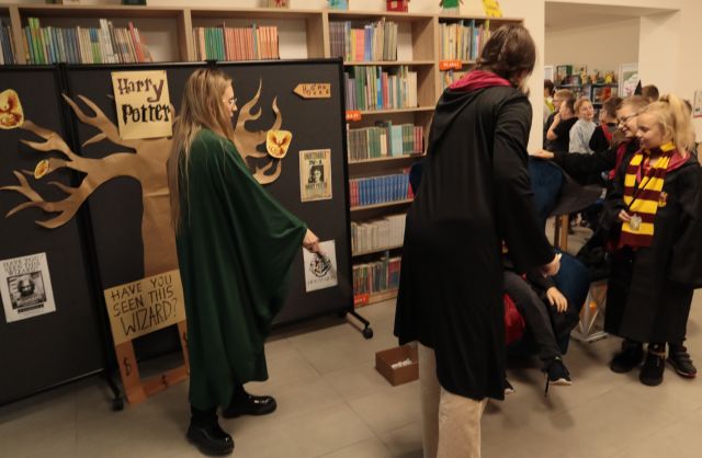 dwie bibliotekarki w pelerynach stoją przed dziećmi w przebranaich z Harry'ego Pottera