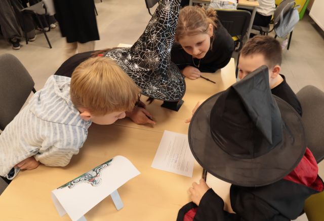 dzieci w przebraniach z Harry'ego Pottera siedzą przy stołach i rozwiązują zadania