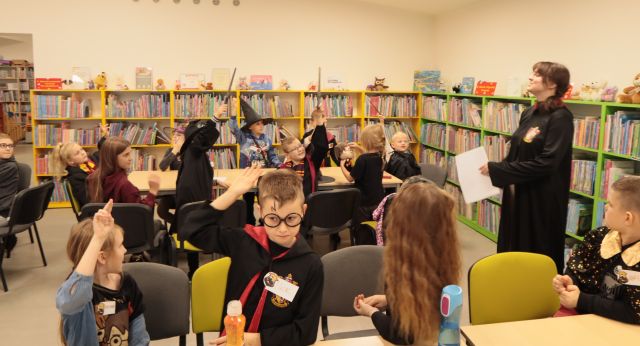dzieci w przebraniach z Harry'ego Pottera siedzą przy stołach i rozwiązują zadania