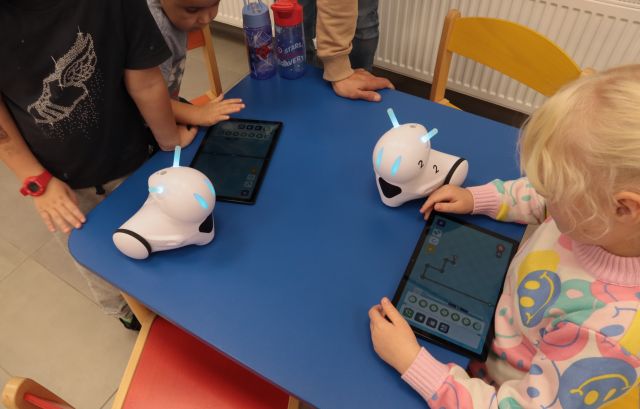 dzieci siedzą przy stoliku, na stoliku dwa roboty Photon