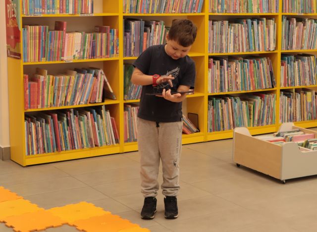 chłopiec trzyma w rękach tablet, w tle regały z książkami