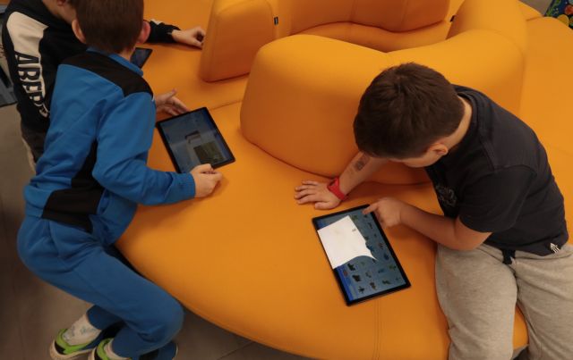 dwóch chłopców siedzi na pomarańczowym siedzisku, grają na tablecie