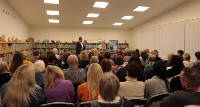 uczestnicy spotkania autorskiego siedzą na krzesłach, w tle prowadzący i autorka