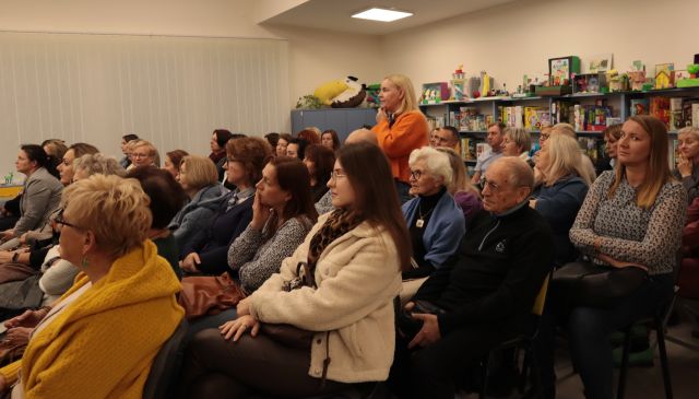 uczestnicy spotkania siedzą na krzesłach, jedna kobieta stoi