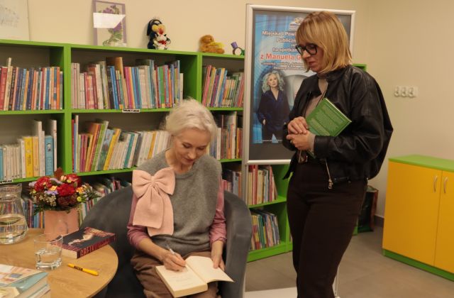 kobieta z książką stoi przed siedzącą i podpisującą książkę Manuelą Gretkowską