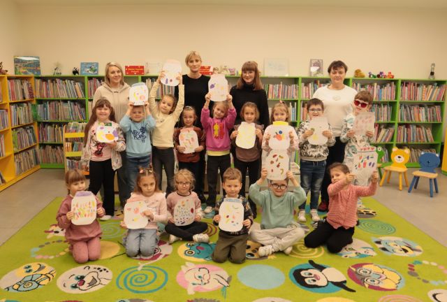 przedszkolaki pozują do zdjęcia ze swoimi pracami plastycznymi, nauczycielkami i bibliotekarką
