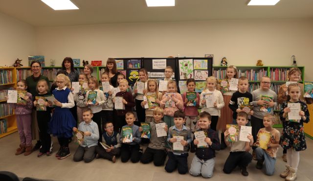 na zdjęciu laureaci konkursu z nagrodami, w tle wystawa prac konkursowych i regały z książkami