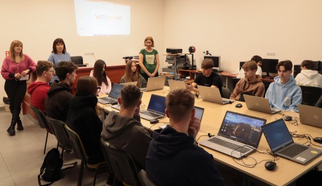 młodzież w sali komputerowej, przed nimi stoi dyrektorka biblioteki i prowadząca szkolenie