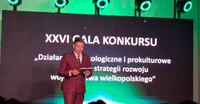 mężczyzna przemawia na tle planszy z nazwą konkursu