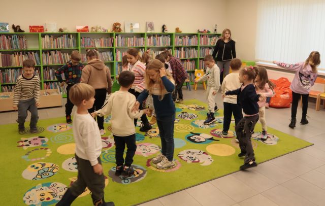 dzieci stoją na zielonym dywanie, w tle regały z książkami