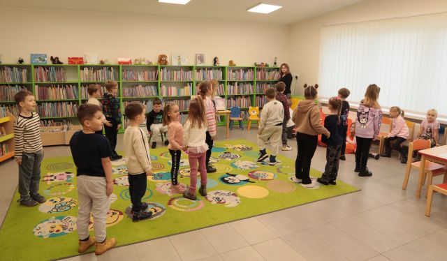 dzieci stoją na zielonym dywanie, w tle regały z książkami