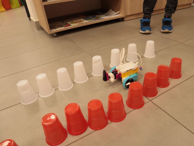 na podłodze ułożone plastikowe kubeczki w kolorach białych i czerwonych, pomiędzy nimi robot z klocków