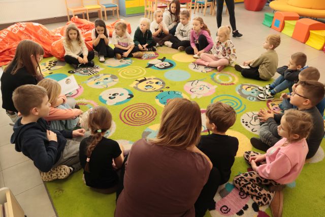 przedszkolaki i bibliotekarka siedzą na zielonym dywanie