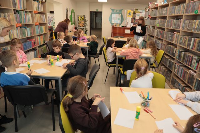 przedszkolaki siedzą przy stołąch i składają kartki