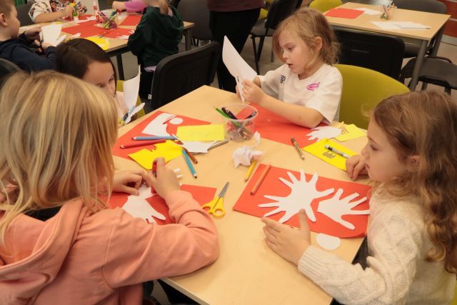 dzieci wycinają i przyklejają odrysowane dłonie na czerwoną kartkę papieru
