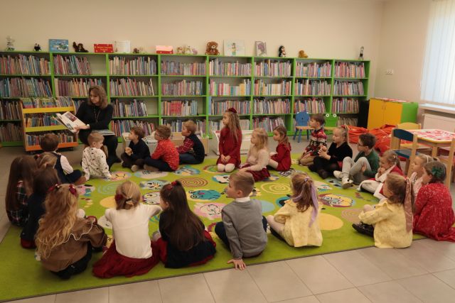 przedszkolaki i bibliotekarka z książką siedzą na dywanie, w tle regały z książkami