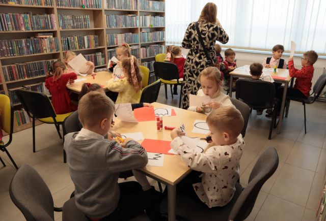 przedszkolaki siedzą przy stołach, wycinają i naklejają czerwone tulipany na białe kartki