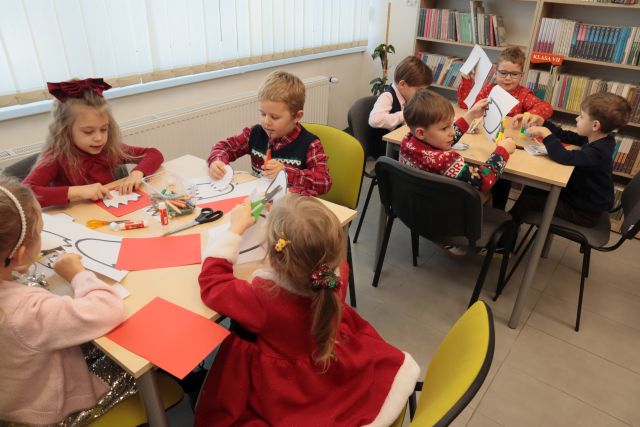 przedszkolaki siedzą przy stołach, wycinają i naklejają czerwone tulipany na białe kartki