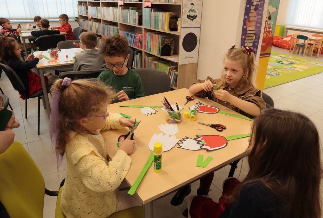 przedszkolaki siedzą przy stołach, wycinają i naklejają czerwone tulipany na białe kartki