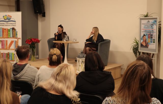 uczestnicy spotkania siedzą na krzesłach, w tle przy stole siedzi autorka z moderatorką