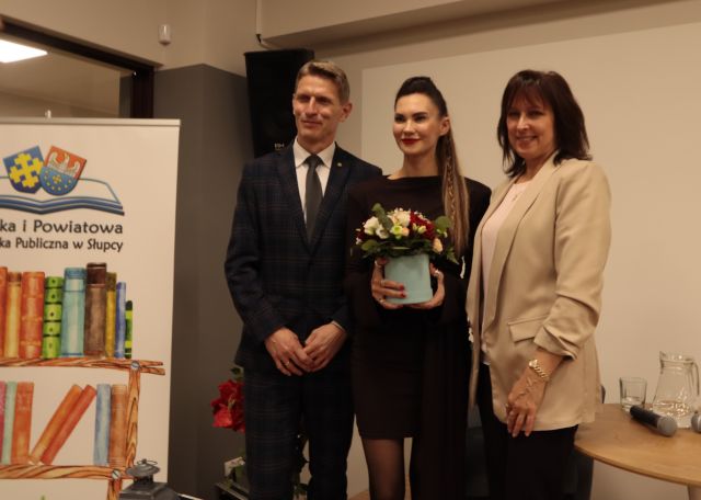 na zdjęciu burmistrz, autorka z kwiatami oraz dyrektorka biblioteki