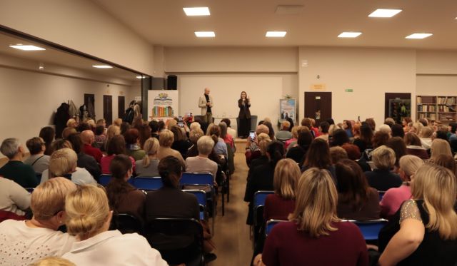 publiczność siedząca na krzesłach, w tle na scenie dr i dziennikarka