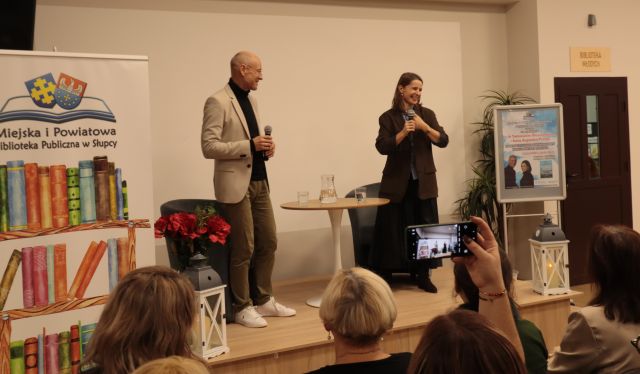 dr i dziennikarka stoją na scenie przed siedzącą publicznością