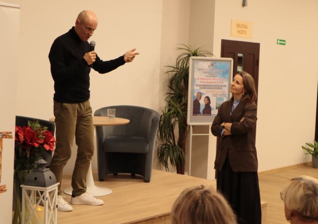 dr na scenie gestykuluje dłonią, dziennikarka stoi przy scenie przodem do doktora