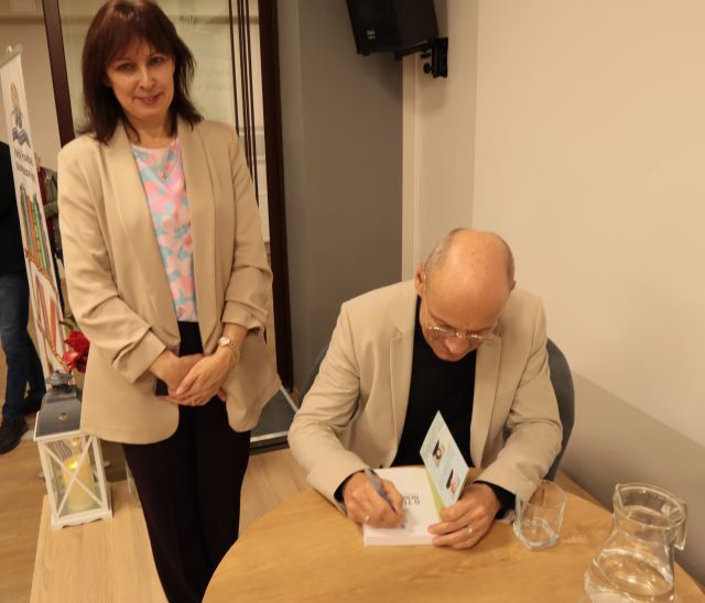 dyrektorka biblioteki stoi przy podpisującym książkę doktorze