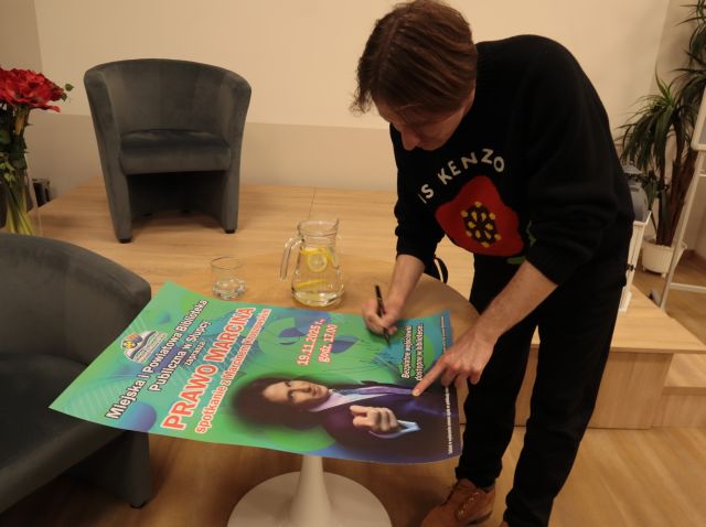 Marcin Kruszewski podpisuje się na plakacie reklamującym spotkanie