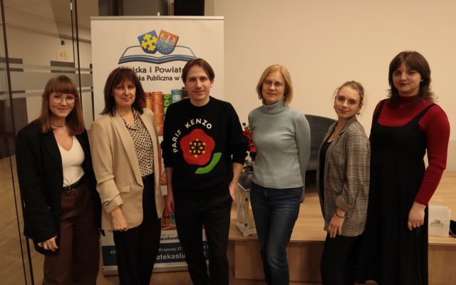 załoga biblioteki pozuje do zdjęcia z Marcinem Kruszewskim