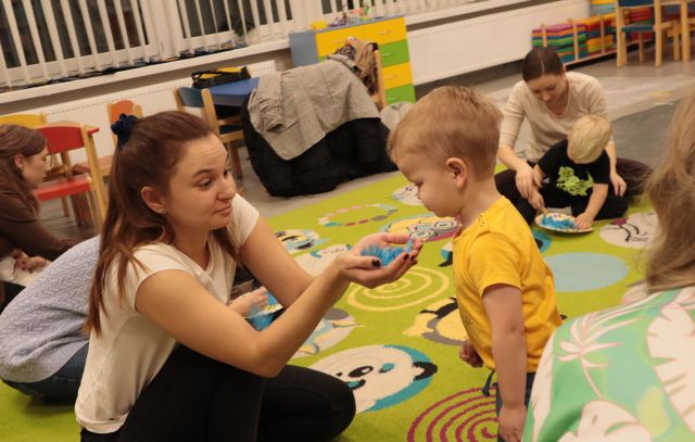 mama na rękach trzyma piórka, w które dmucha chłopiec